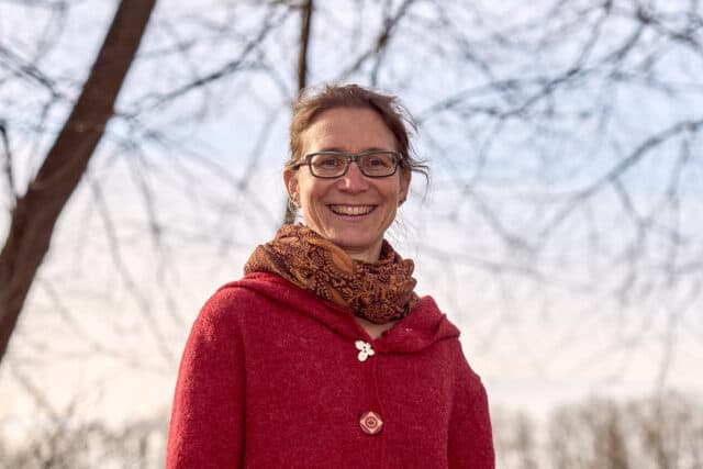 Frau lächelt in roter Jacke, natürlicher Hintergrund.