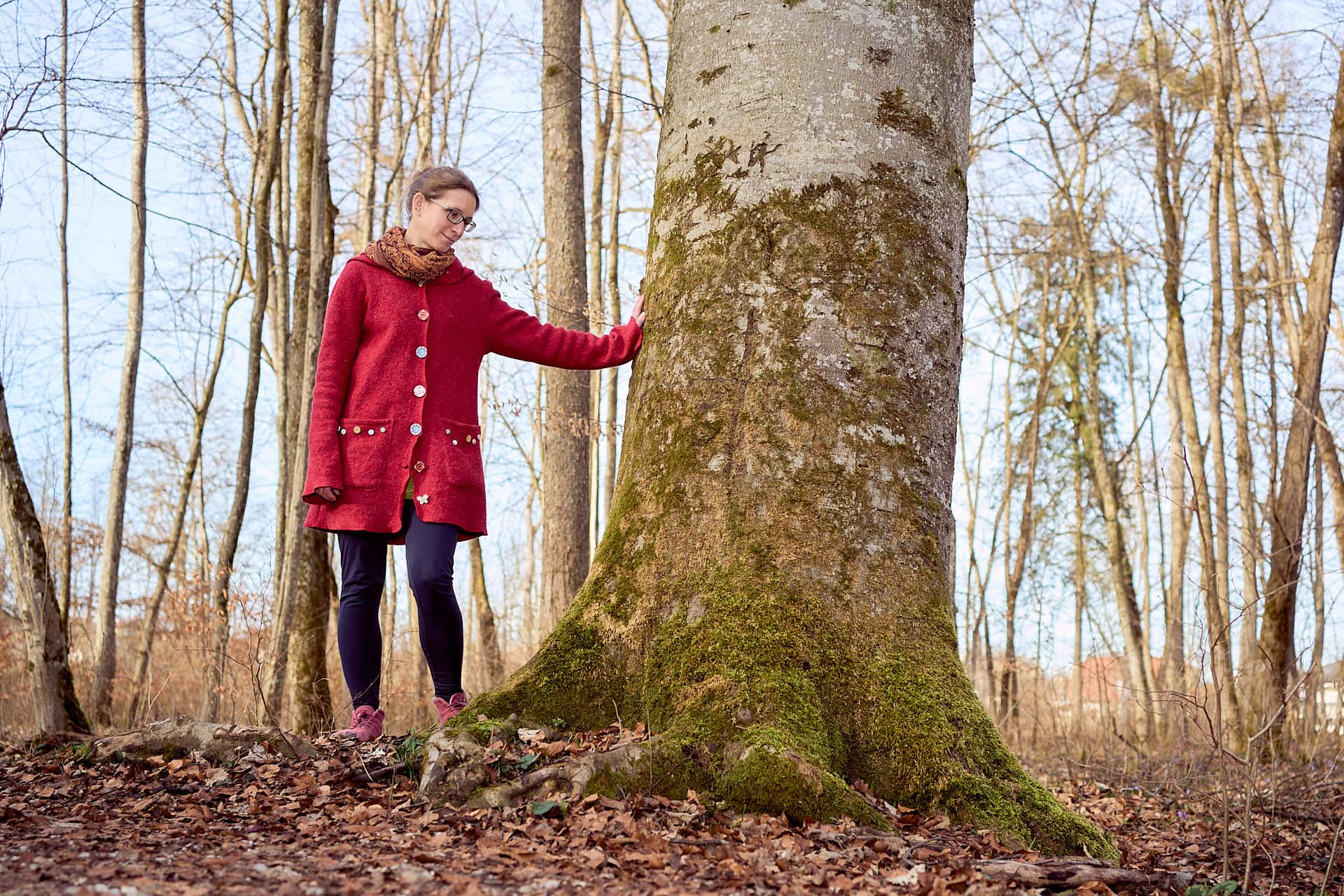 Frau berührt Baum im sonnigen Wald.